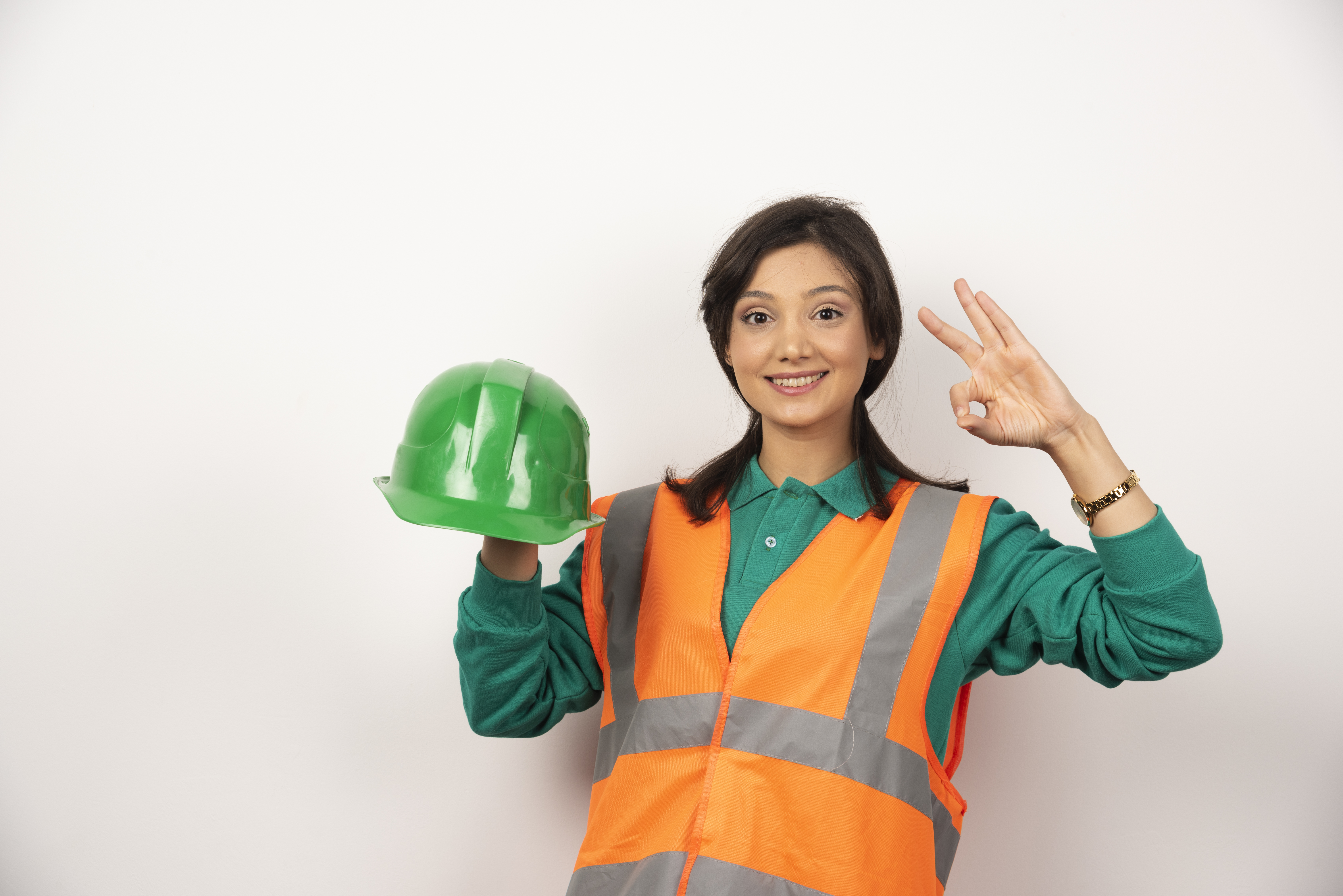 Female engineer showing ok gesture and holding a helmet on white background