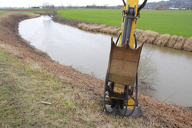 An excavator tool used for cutting wild plant growth along a canal.