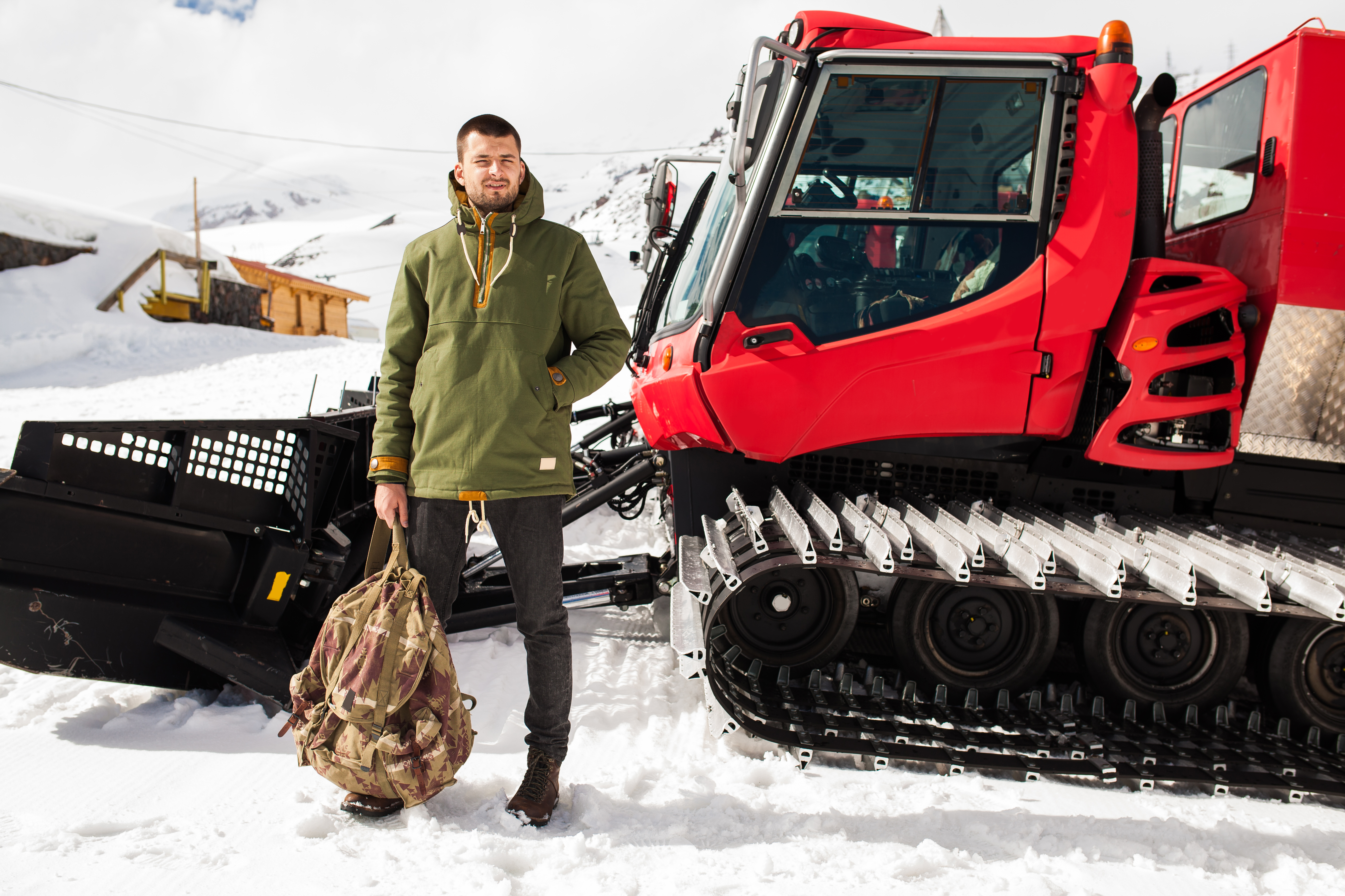 young hipster man hiking in mountains, winter vacation traveling, north, snow, warm clothes, anorak, jeans, boots, snowcat